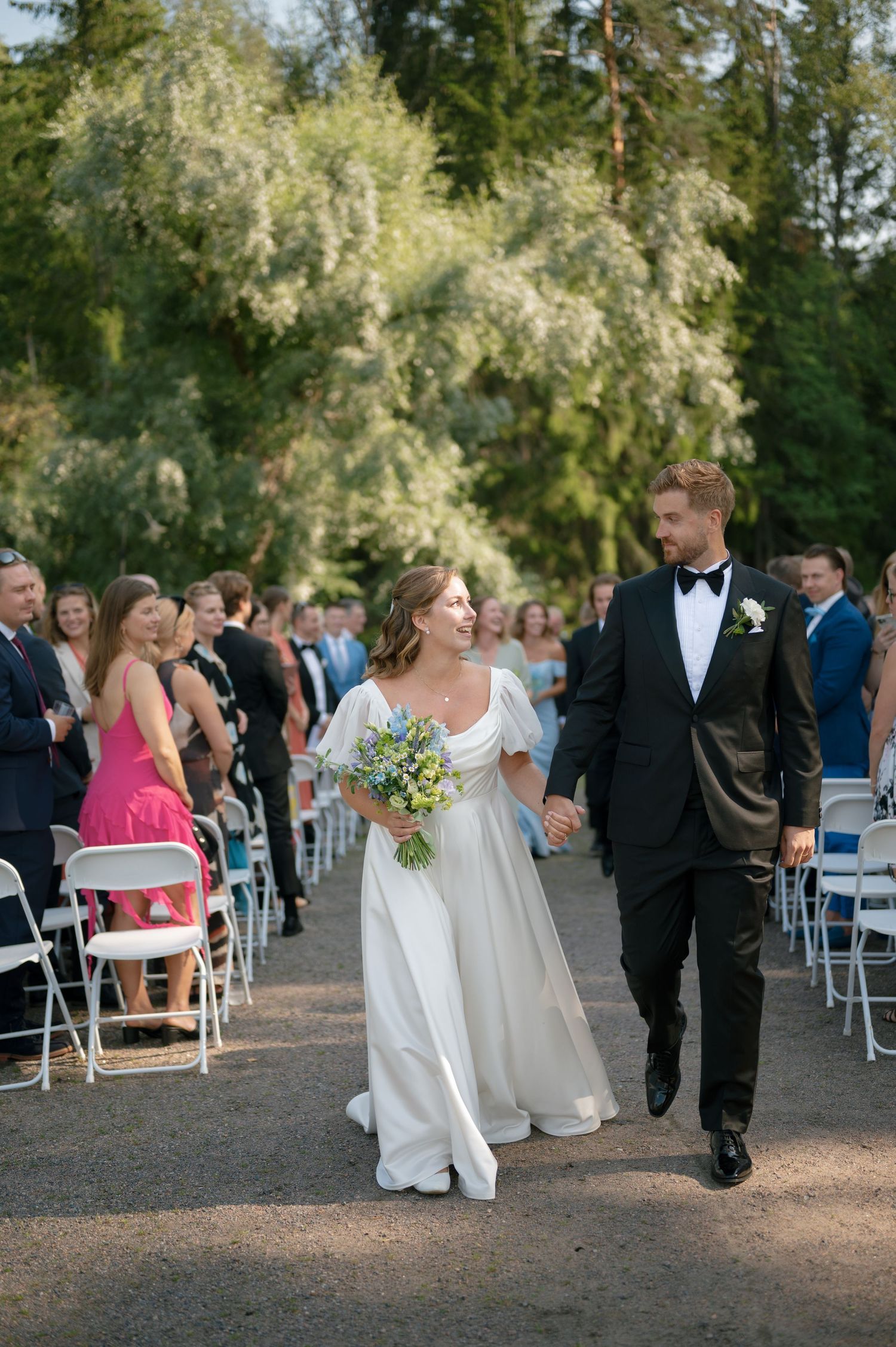 Wedding party members walk down a tree-lined path after the ceremony.