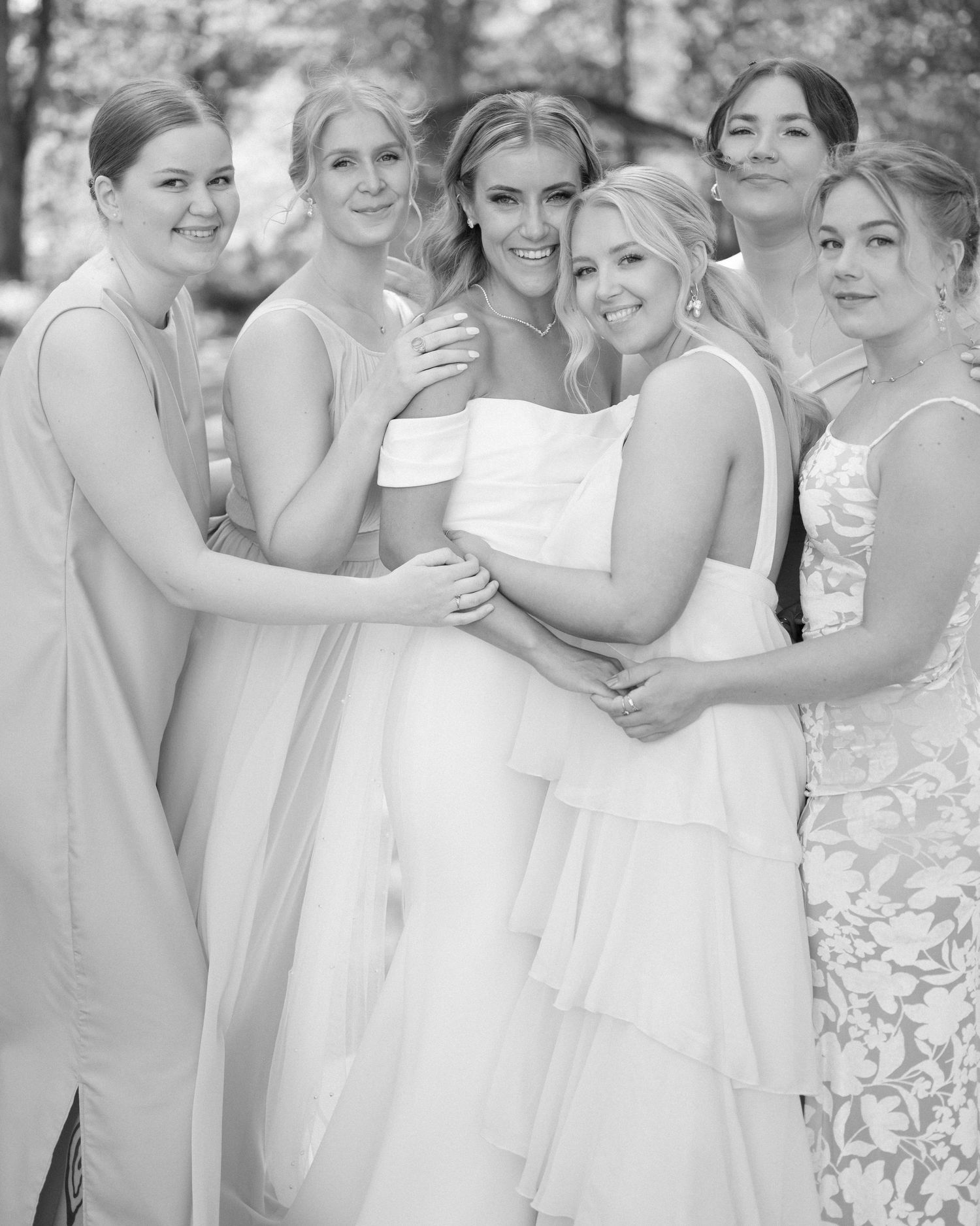 Candid moment of bridal party laughing together in pink and white dresses outdoors.