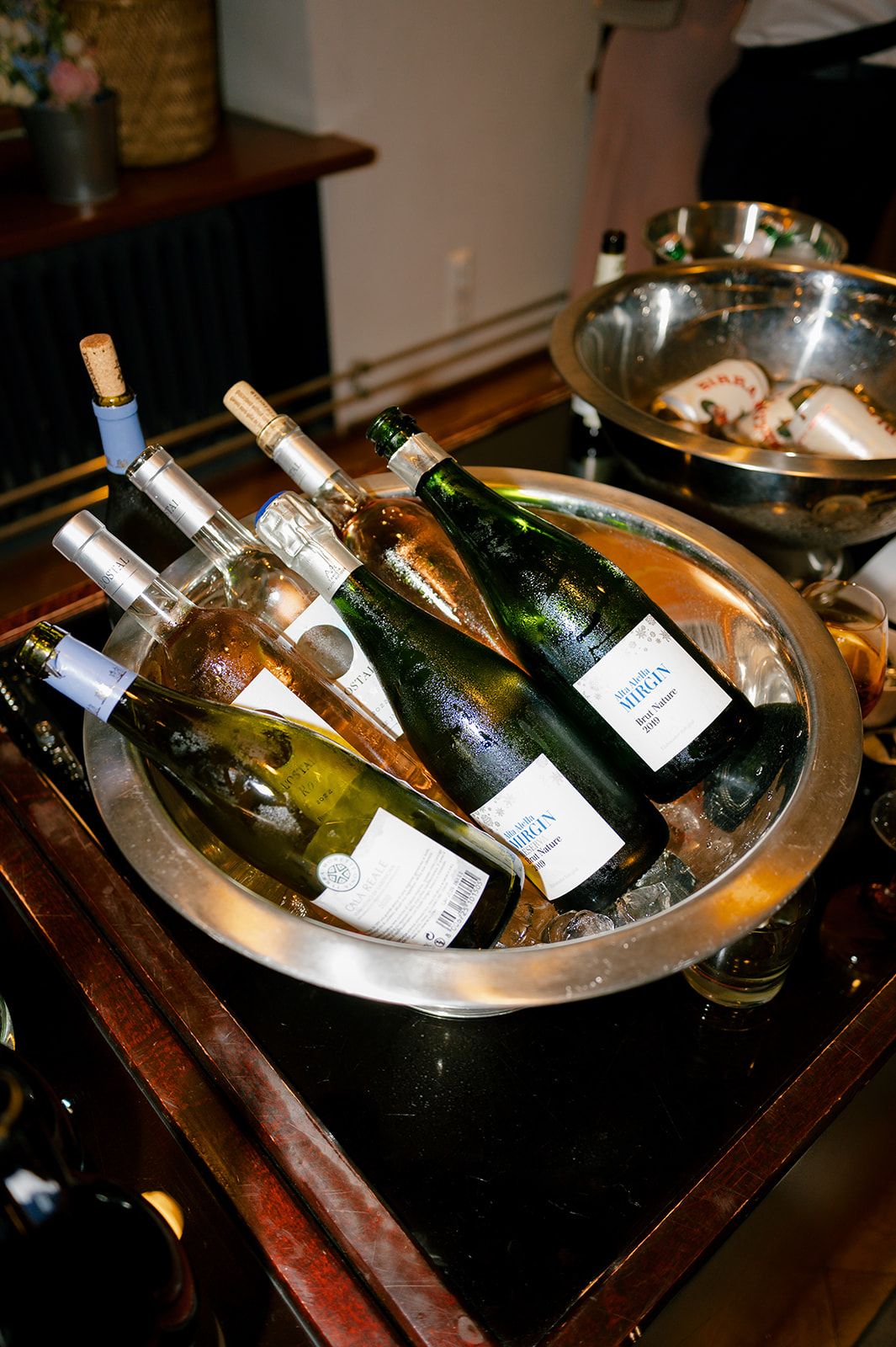 Wine bottles chilling in an ice bucket on a wooden bar cart with serving dishes.