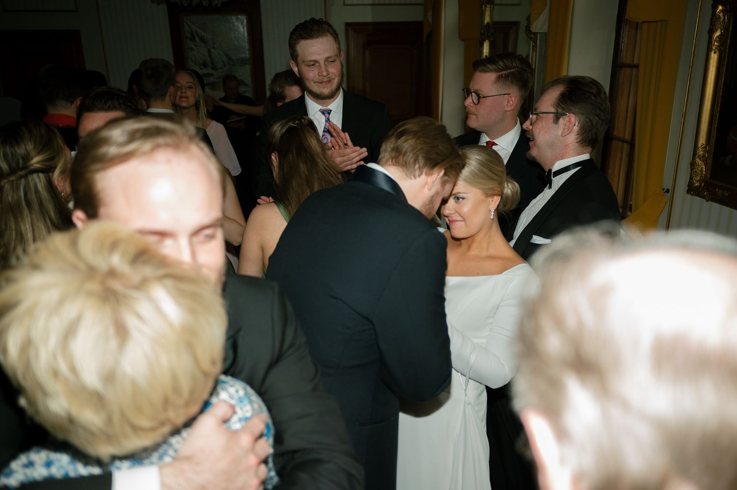A formal event shows people in suits and formal attire mingling and conversing in an elegant indoor setting.
