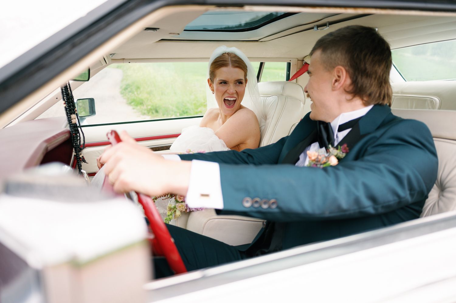 A couple shares a joyful moment while sitting in a car together dressed in formal attire.