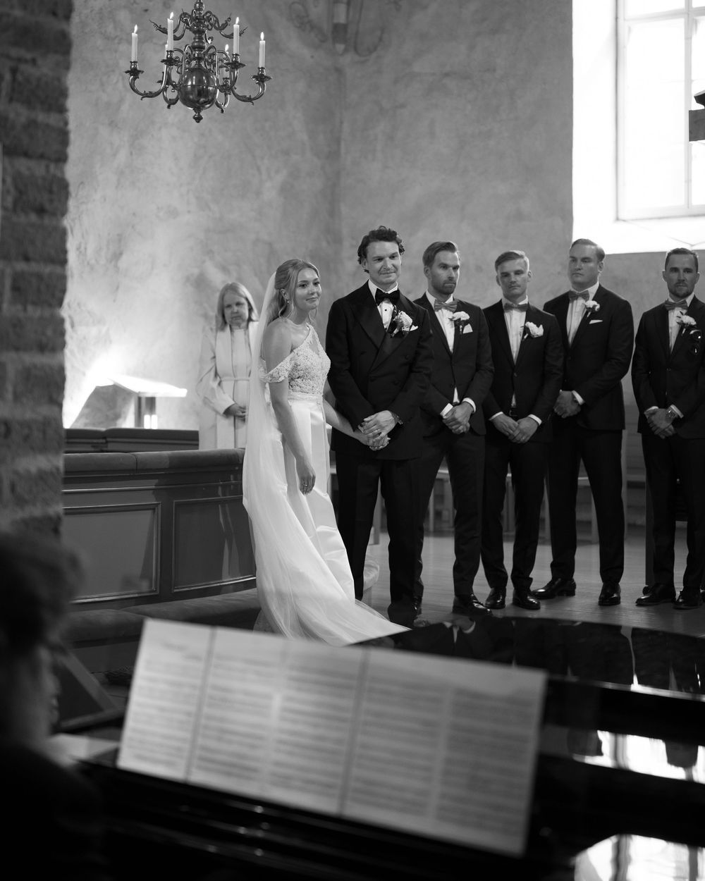 Black and white photo of a wedding ceremony with groomsmen in tuxedos standing in a church.