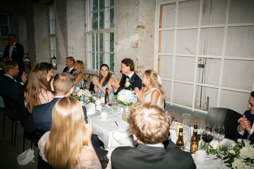 Wedding reception venue with exposed brick walls and large windows filled with celebrating guests.