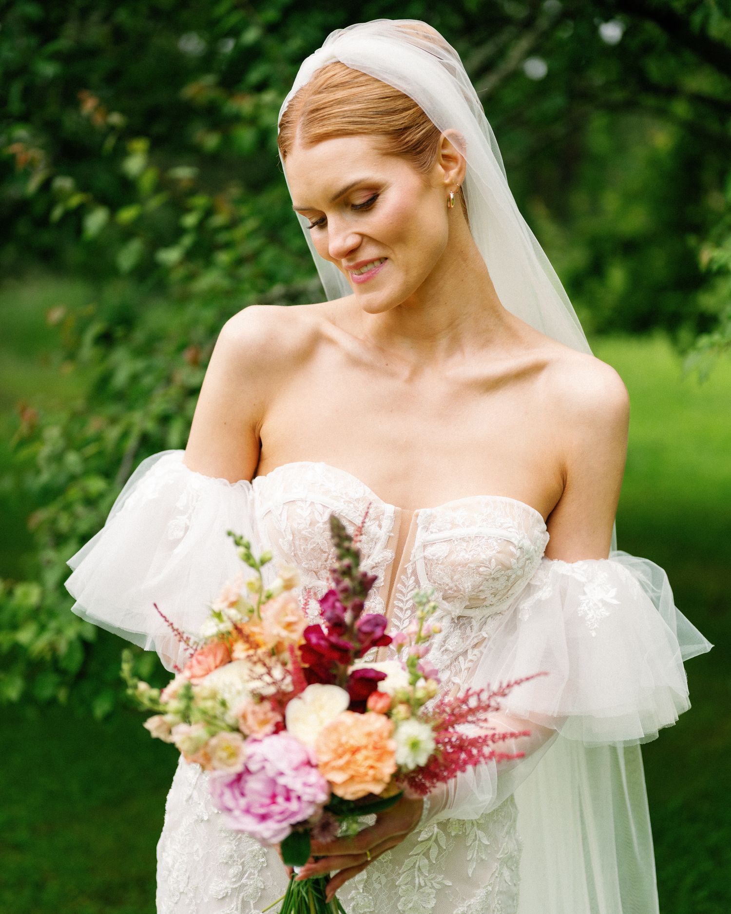 Bride holds a vibrant bouquet featuring pink and peach flowers against her white wedding gown.