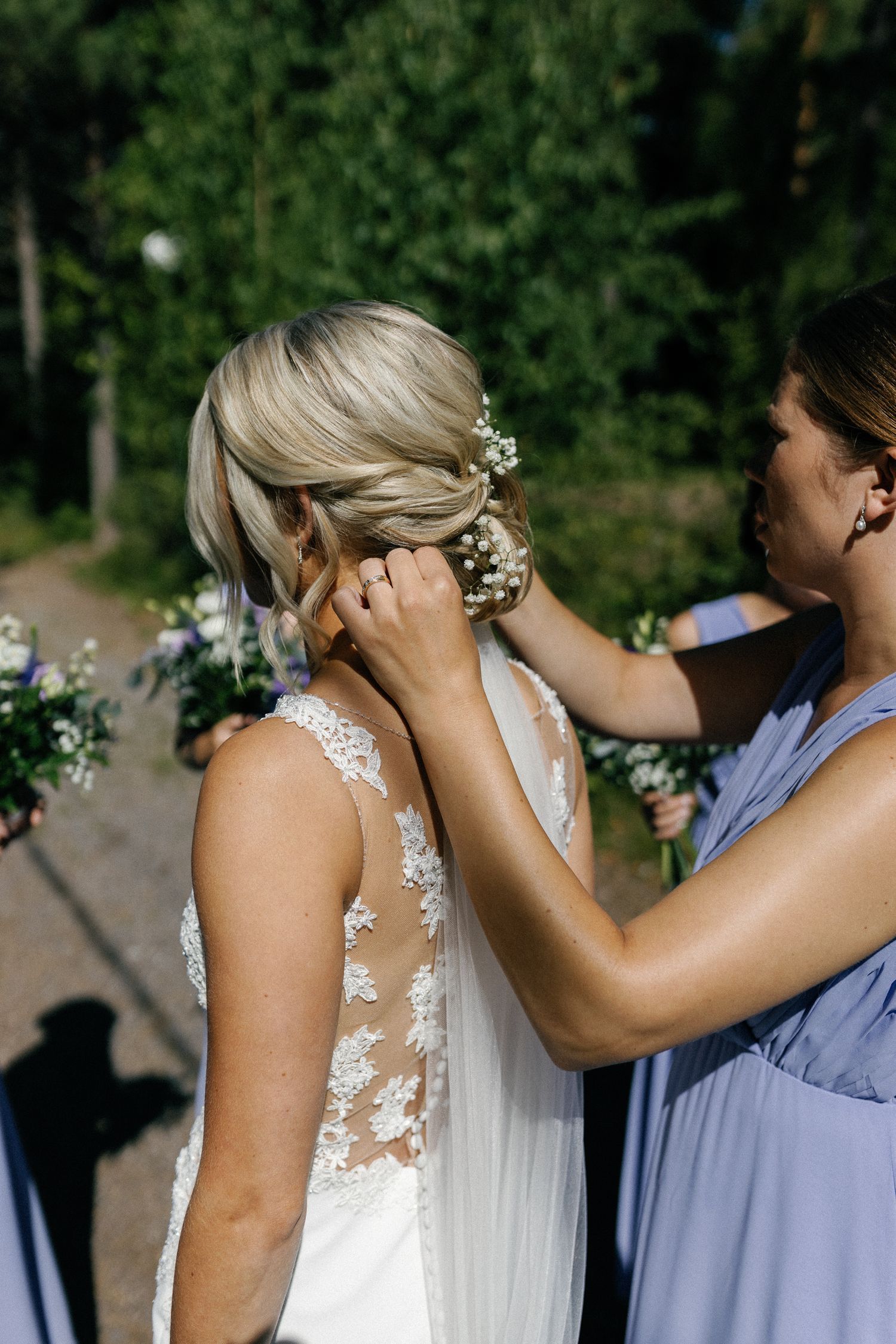 Bridesmaids in lavender dresses help adjust the bride's veil during wedding preparations.