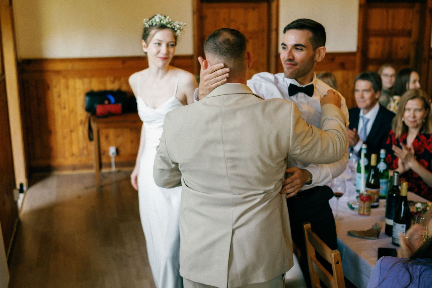 Wedding reception guests enjoying drinks and conversation in a rustic wood-paneled venue.
