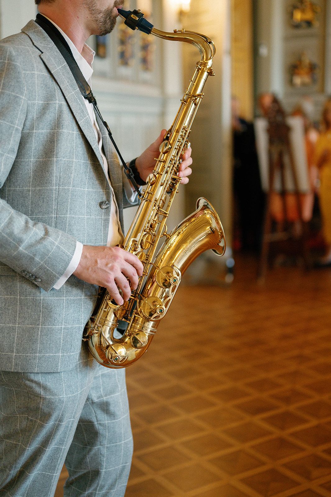 Musician playing saxophone in a grey checkered suit at an event venue.