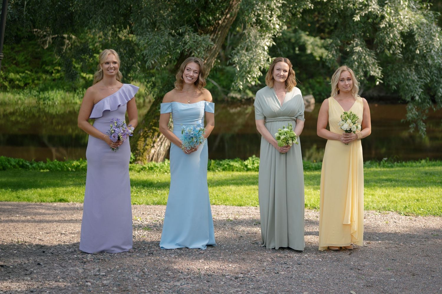 Bridesmaids in pastel dresses stand together during outdoor wedding celebration.