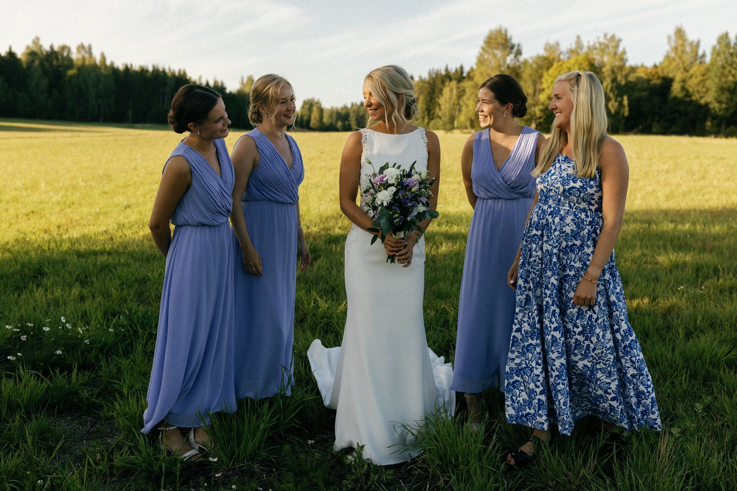 Wedding party in blue bridesmaid dresses poses together in outdoor field setting.