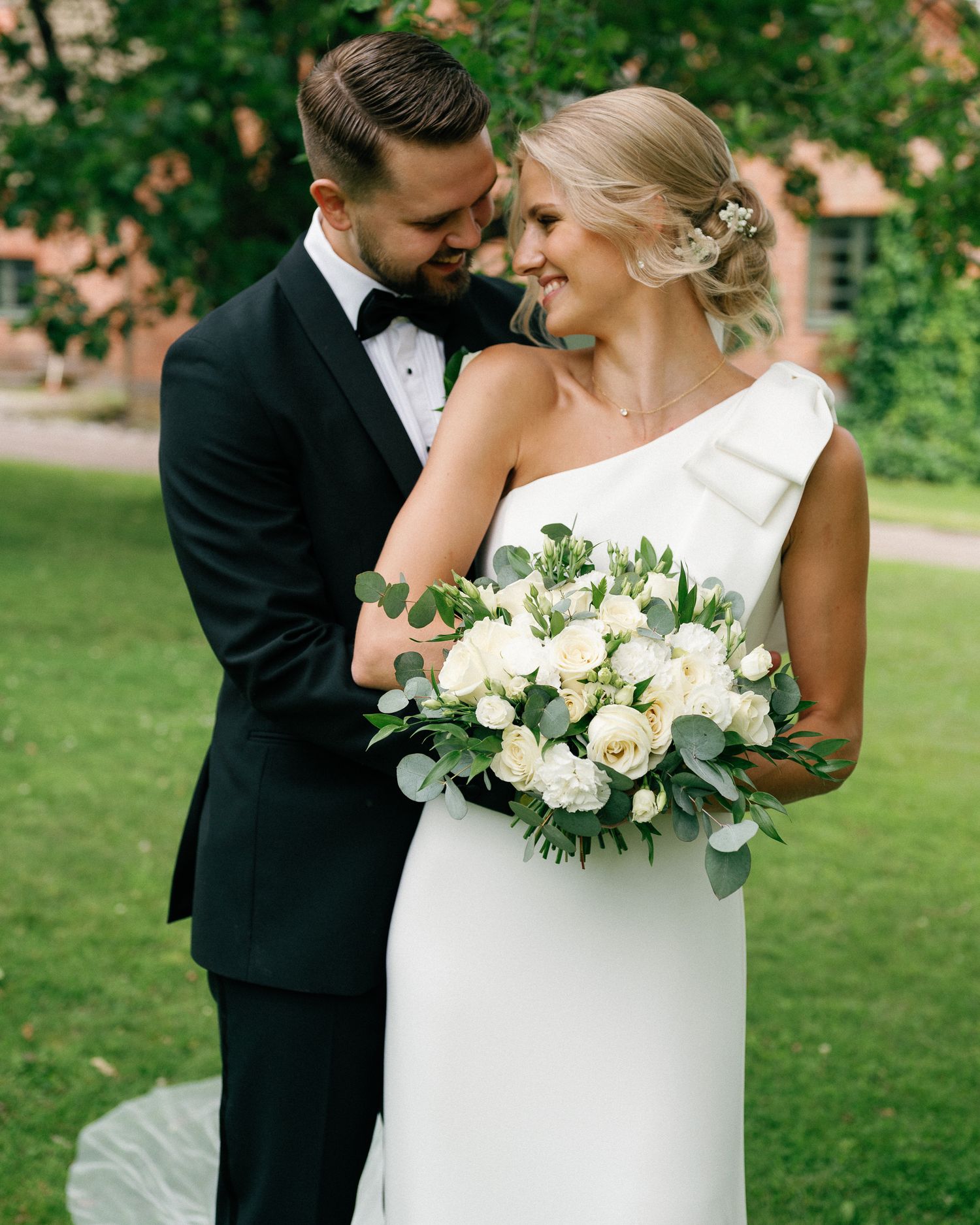 Newlywed couple sharing intimate moments in a garden setting with white floral bouquet.