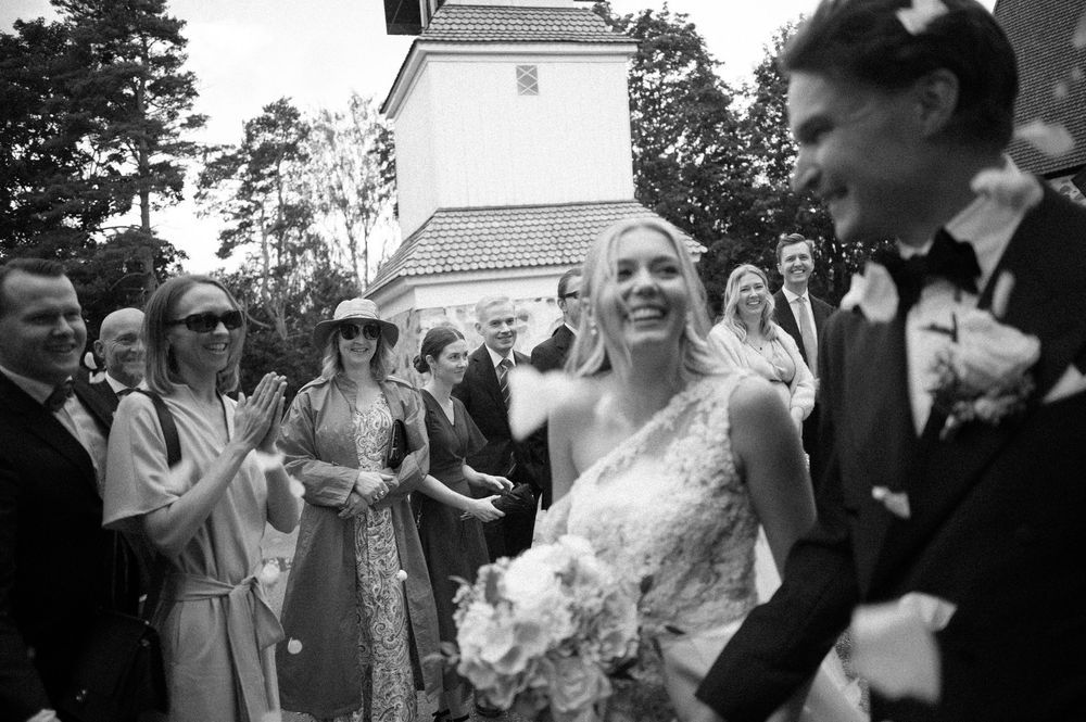 Wedding party exits stone church while guests celebrate with confetti.