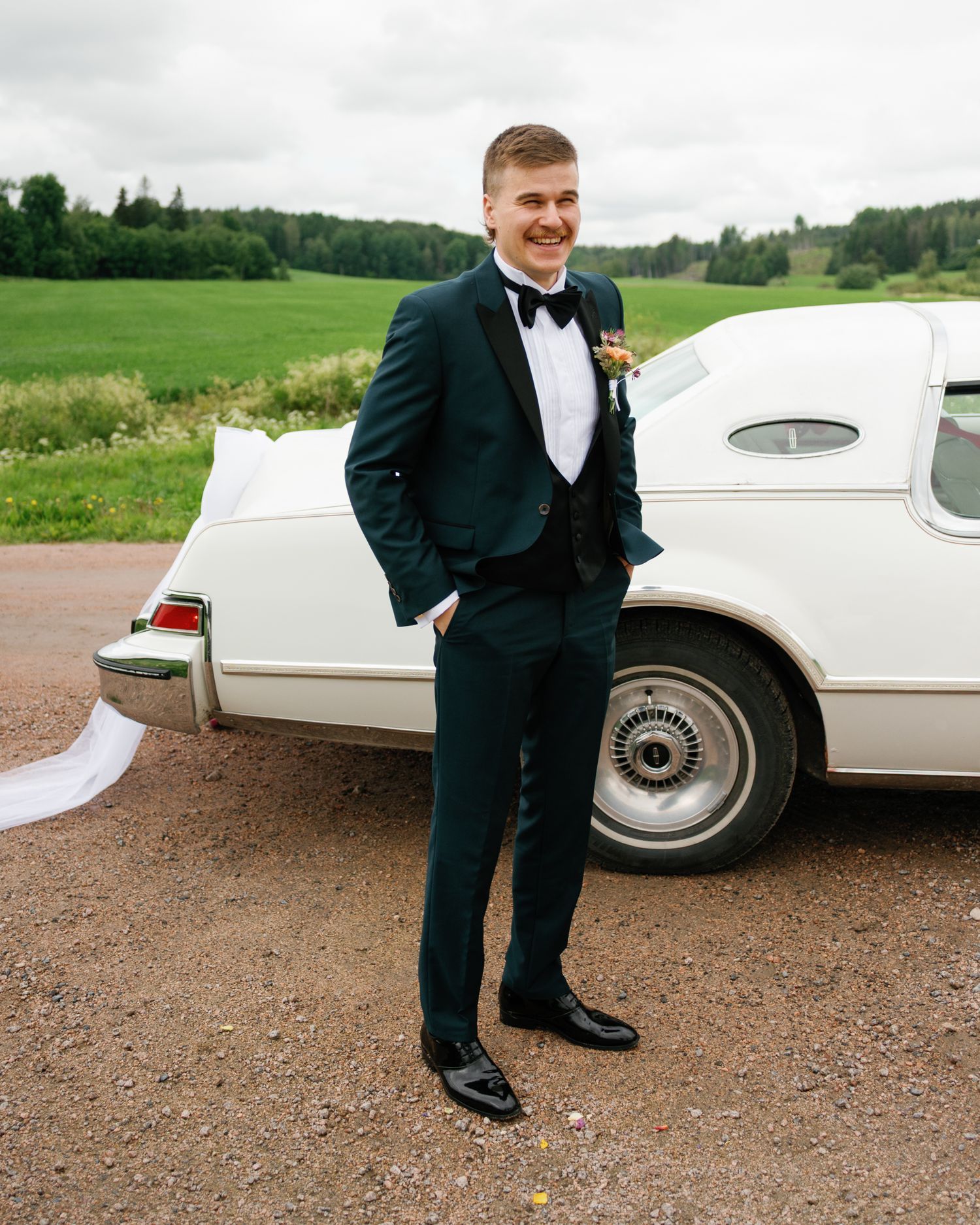 Vintage white car parked on gravel with elegant wedding details visible.