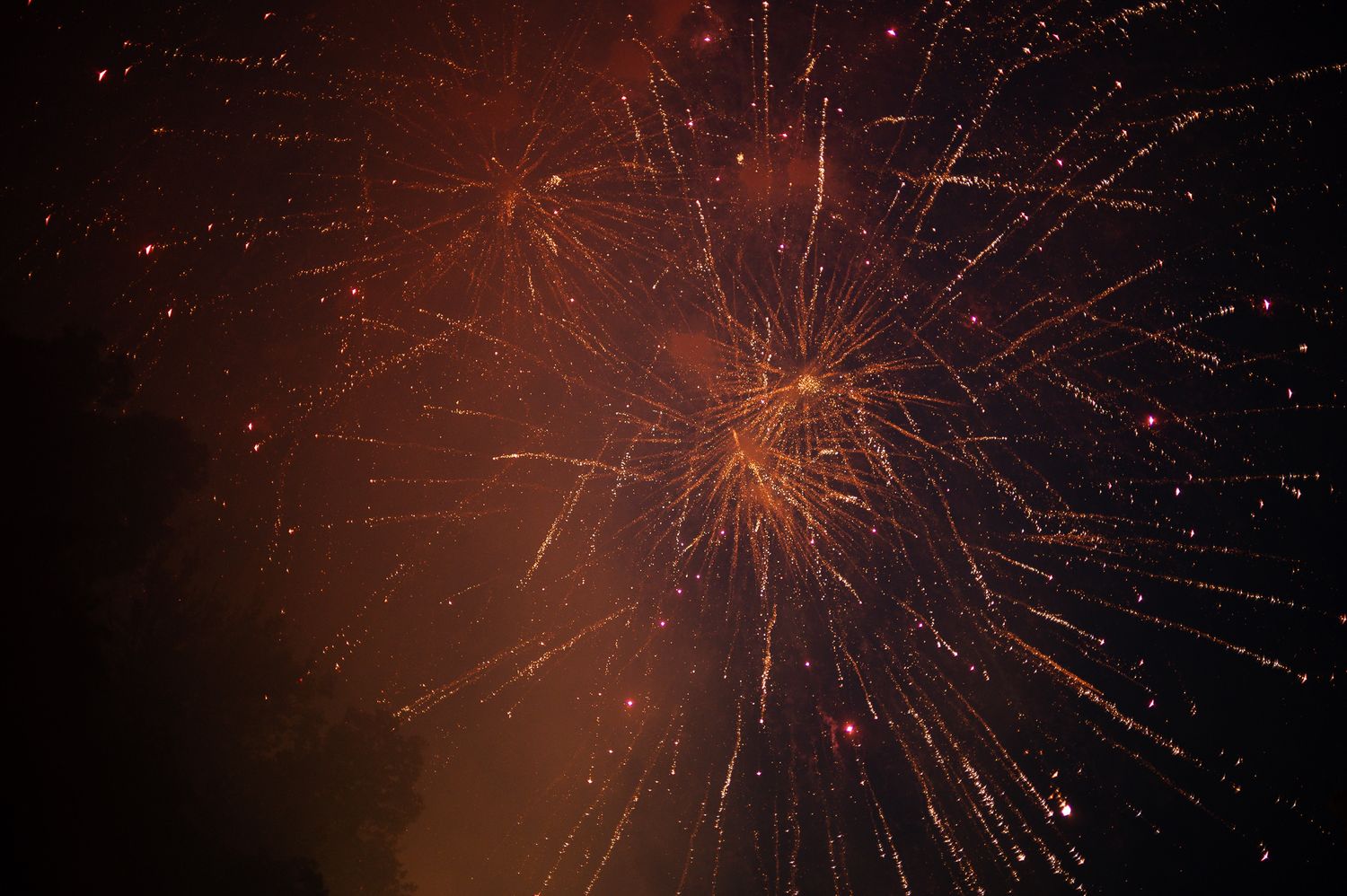 Vibrant red and orange fireworks exploding against a dark night sky in a dazzling display of light.