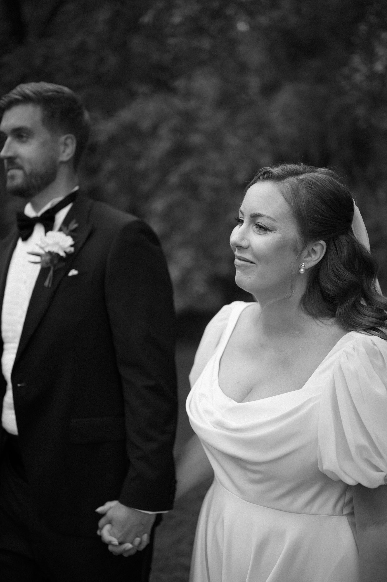 Black and white portrait of a couple in formal wedding attire against a natural backdrop.