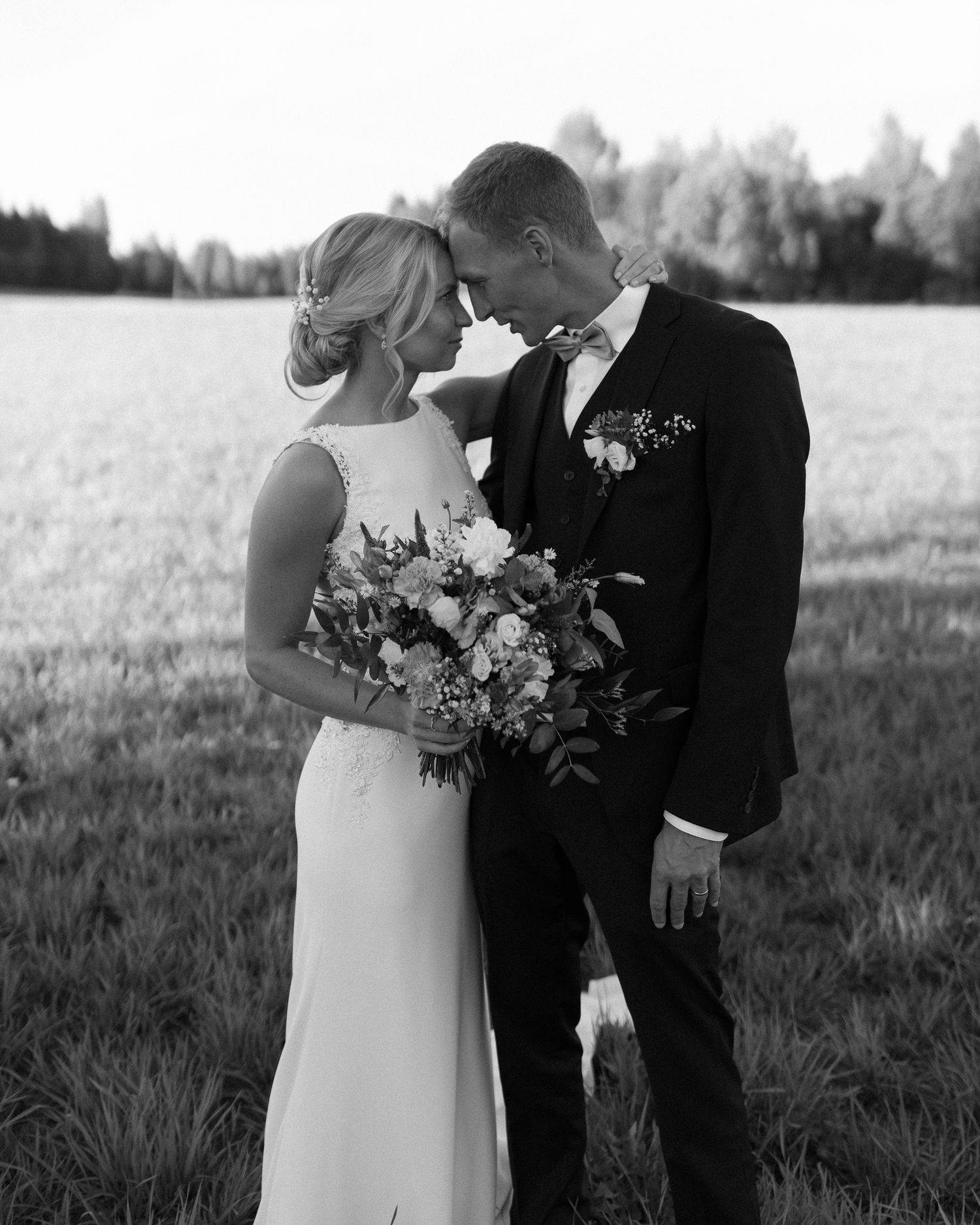 Intimate black and white portrait of couple with bridal bouquet against natural landscape.
