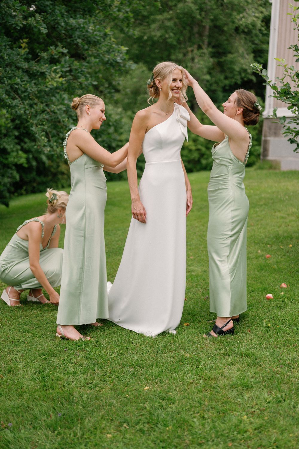 Wedding party helps adjust the bride's dress during outdoor preparations in sage green bridesmaid dresses.