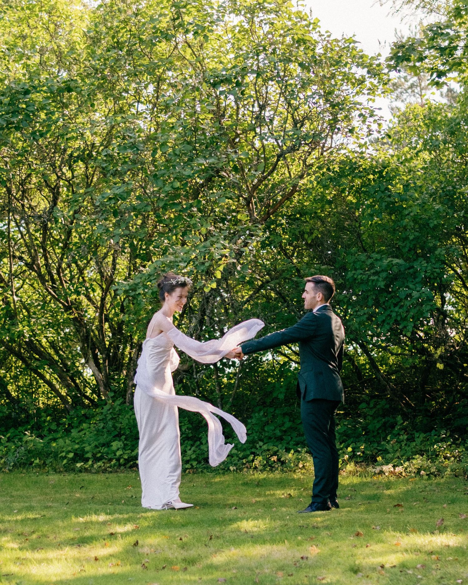 Playful wedding couple dancing and twirling in a sun-dappled garden setting.