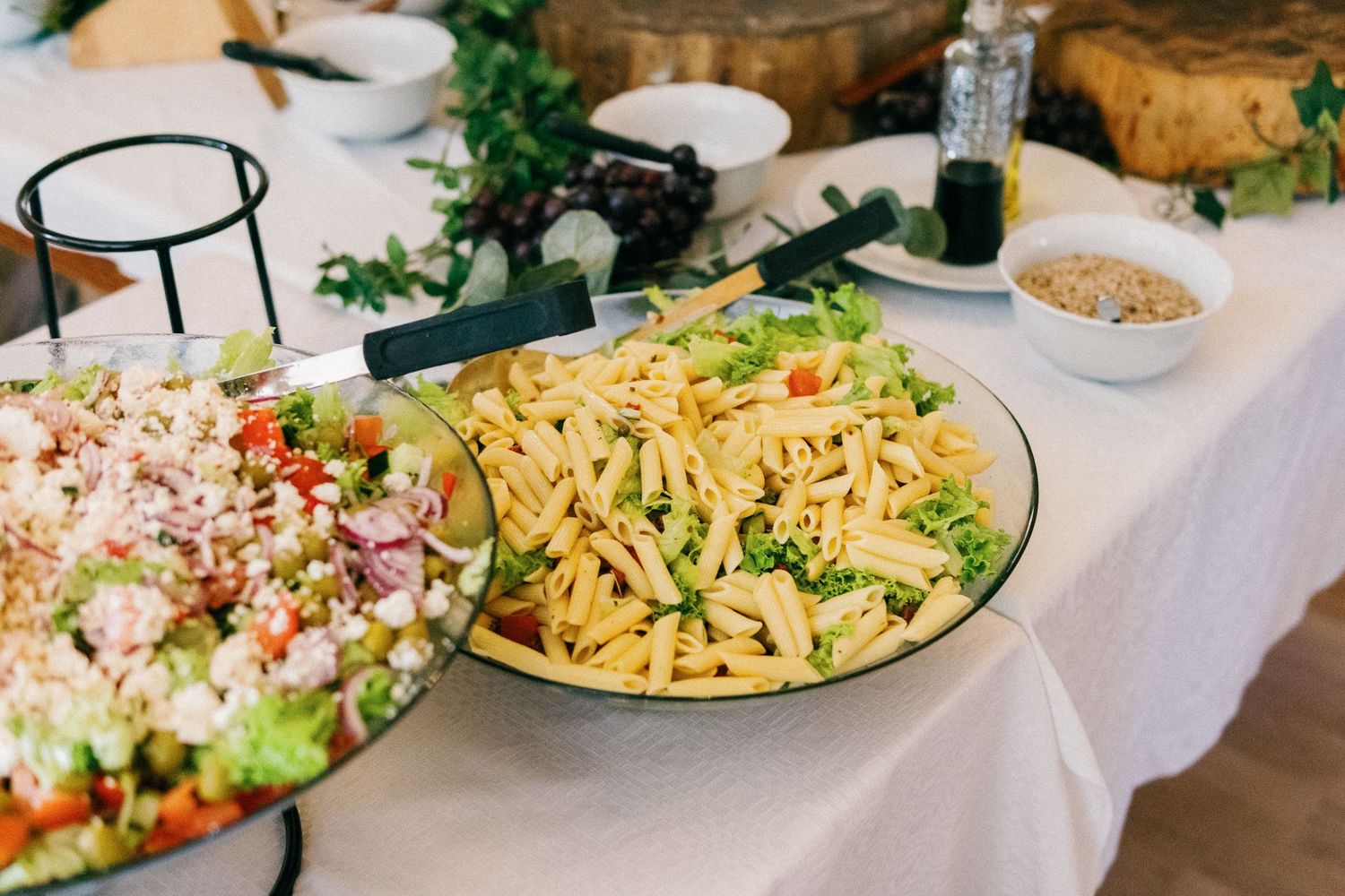 Elegant wedding buffet spread featuring colorful salads and pasta dishes on a white tablecloth.