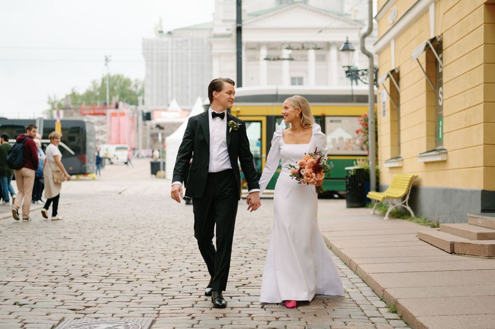 A wedding couple walking along a cobblestone street in formal attire.