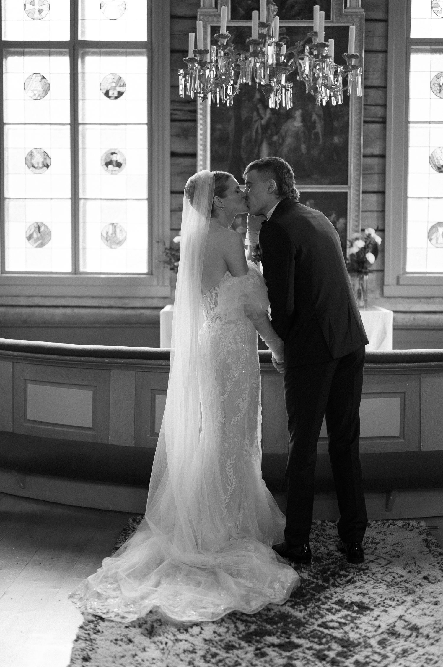 Romantic wedding couple shares intimate moments in an elegant room with crystal chandeliers and decorative windows.