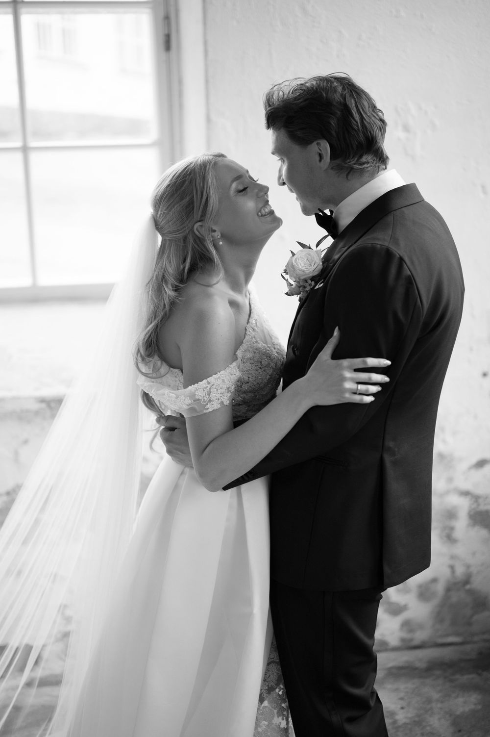 An intimate black and white portrait of newlyweds sharing a tender moment in front of a window.