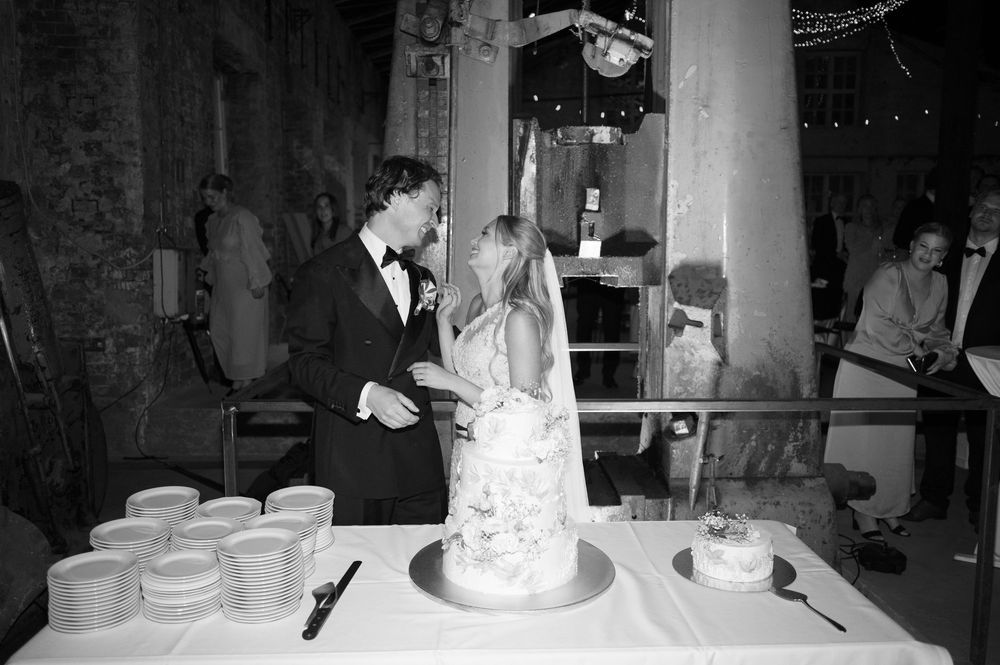 A tiered wedding cake sits on a white table with elegant decorations and place settings.