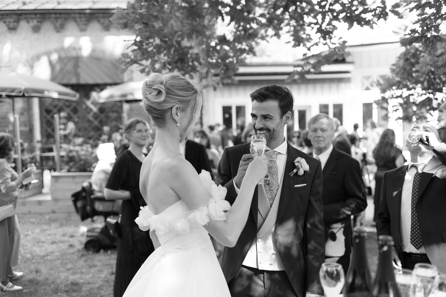 Black and white photo of a bride and groom sharing a microphone during their outdoor wedding reception.