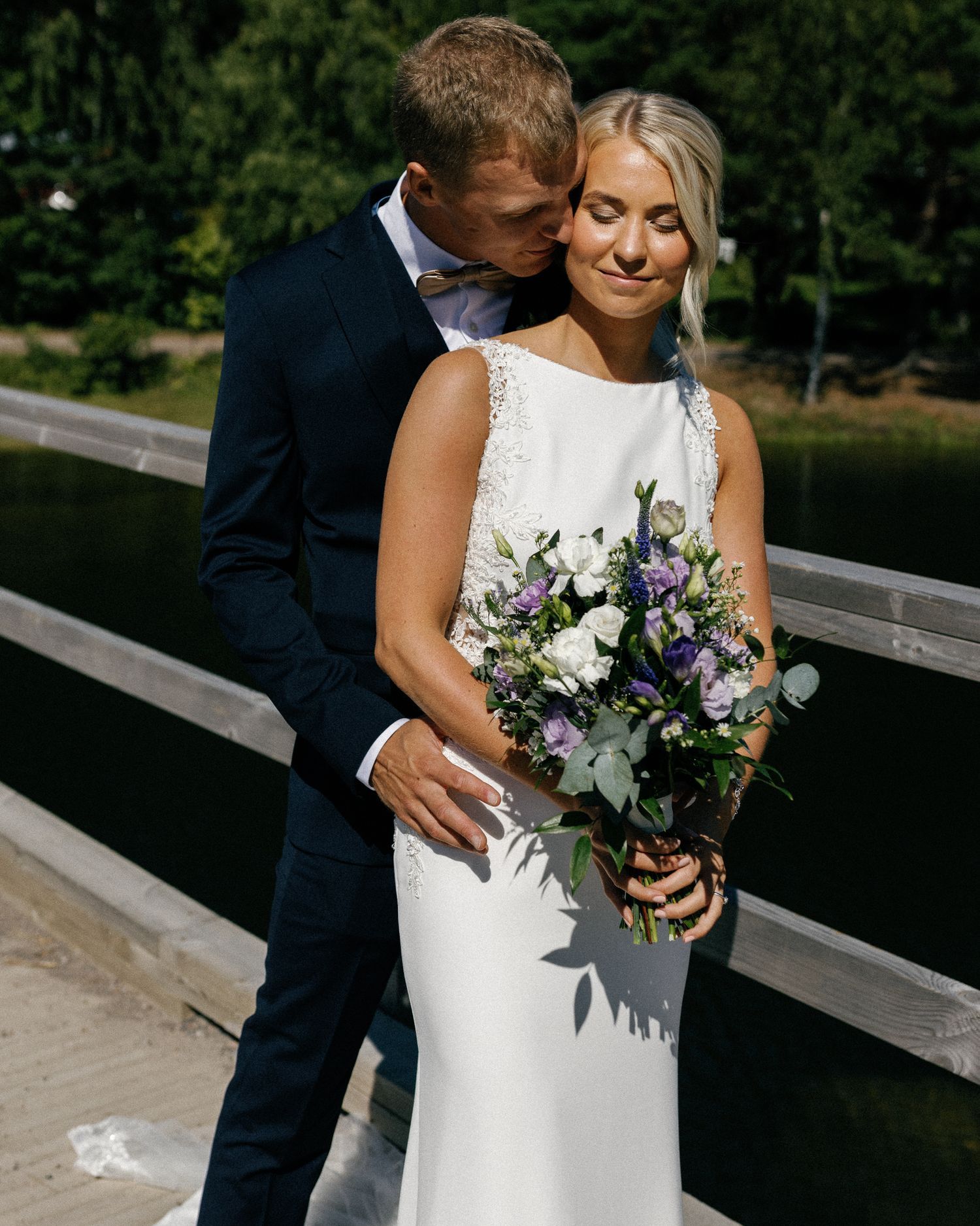 Close-up wedding photo showing details of a white bridal gown and purple bouquet.
