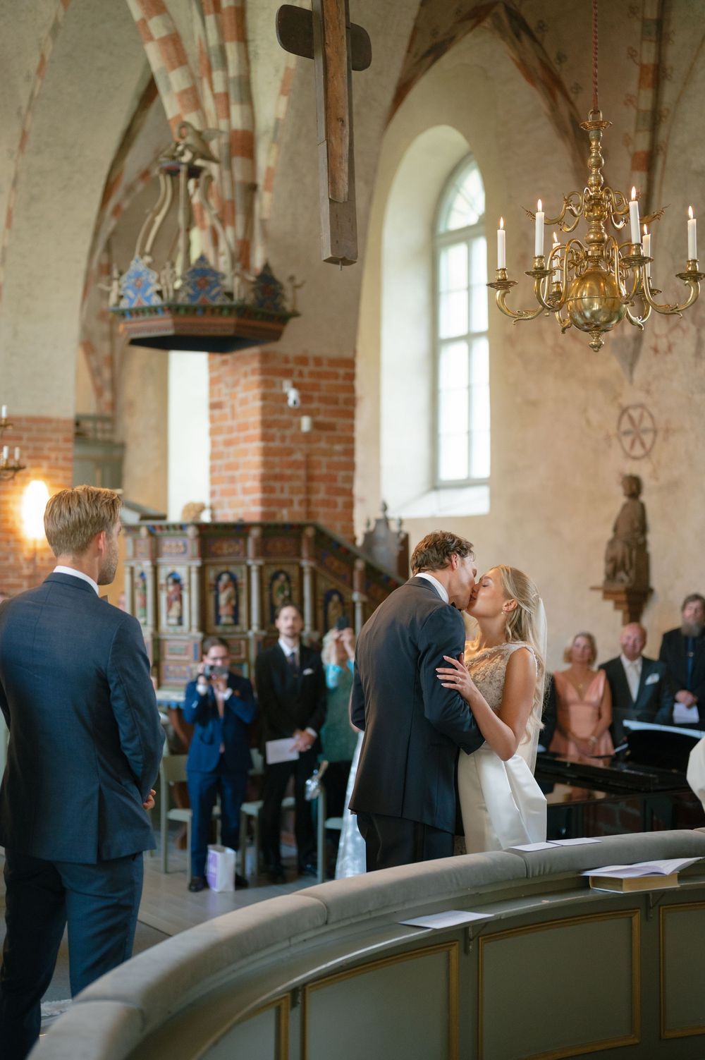 A romantic first kiss during a wedding ceremony in a traditional church with exposed brick walls.