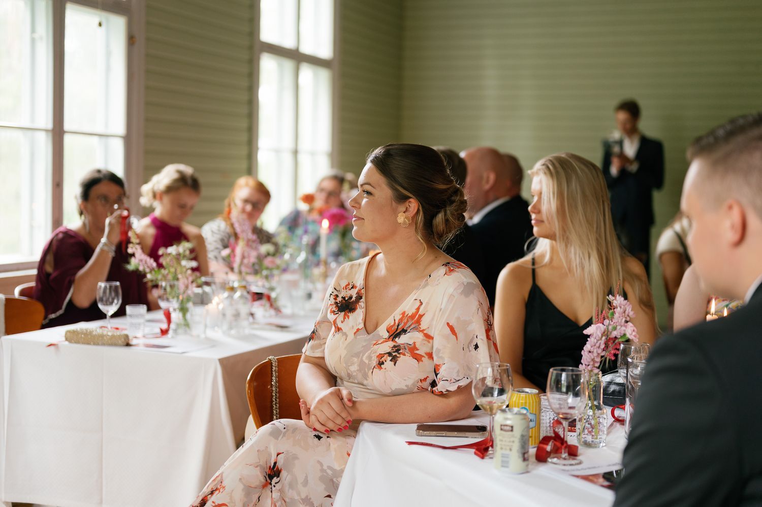 Wedding reception venue with guests seated at decorated tables by large windows.