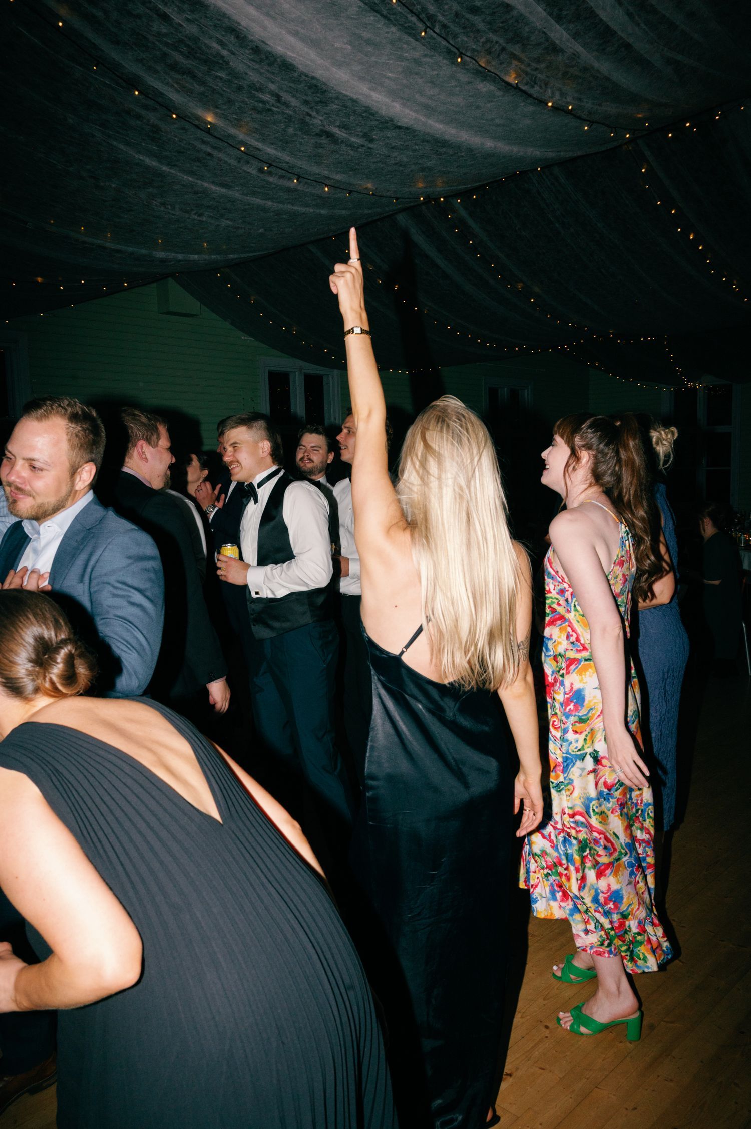 Wedding guests dancing and celebrating on dimly lit dance floor.
