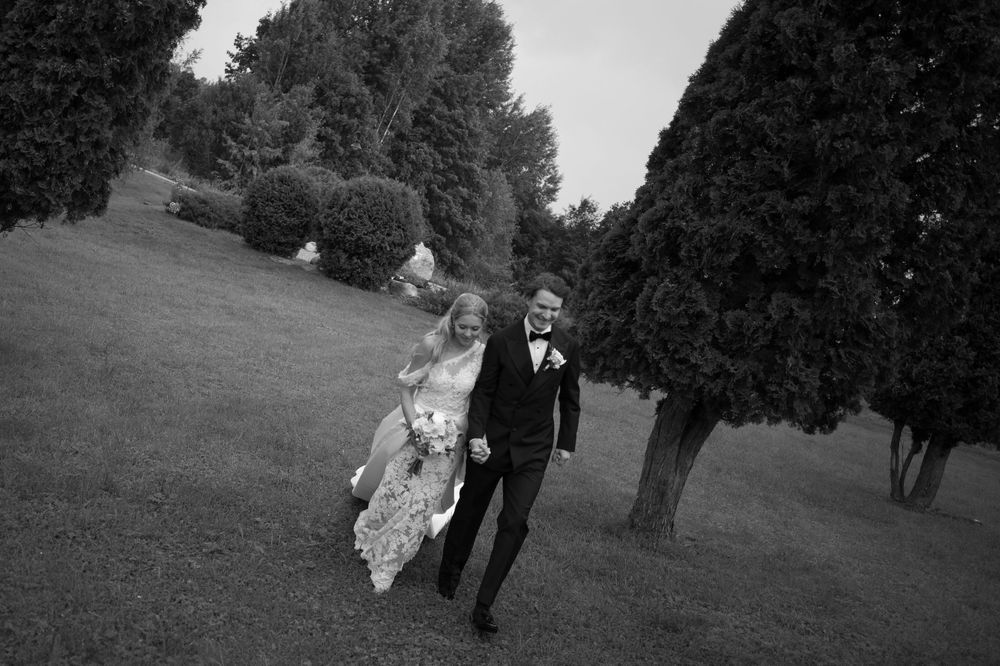 Newlyweds stroll through a scenic outdoor setting with dramatic trees in the background.