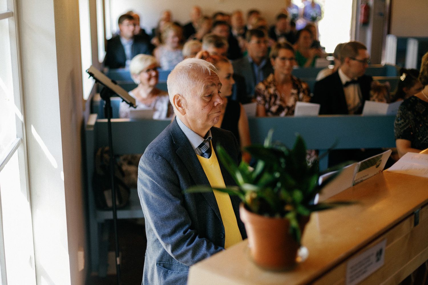 A speaker in a bow tie addresses the congregation from a wooden podium in a church.
