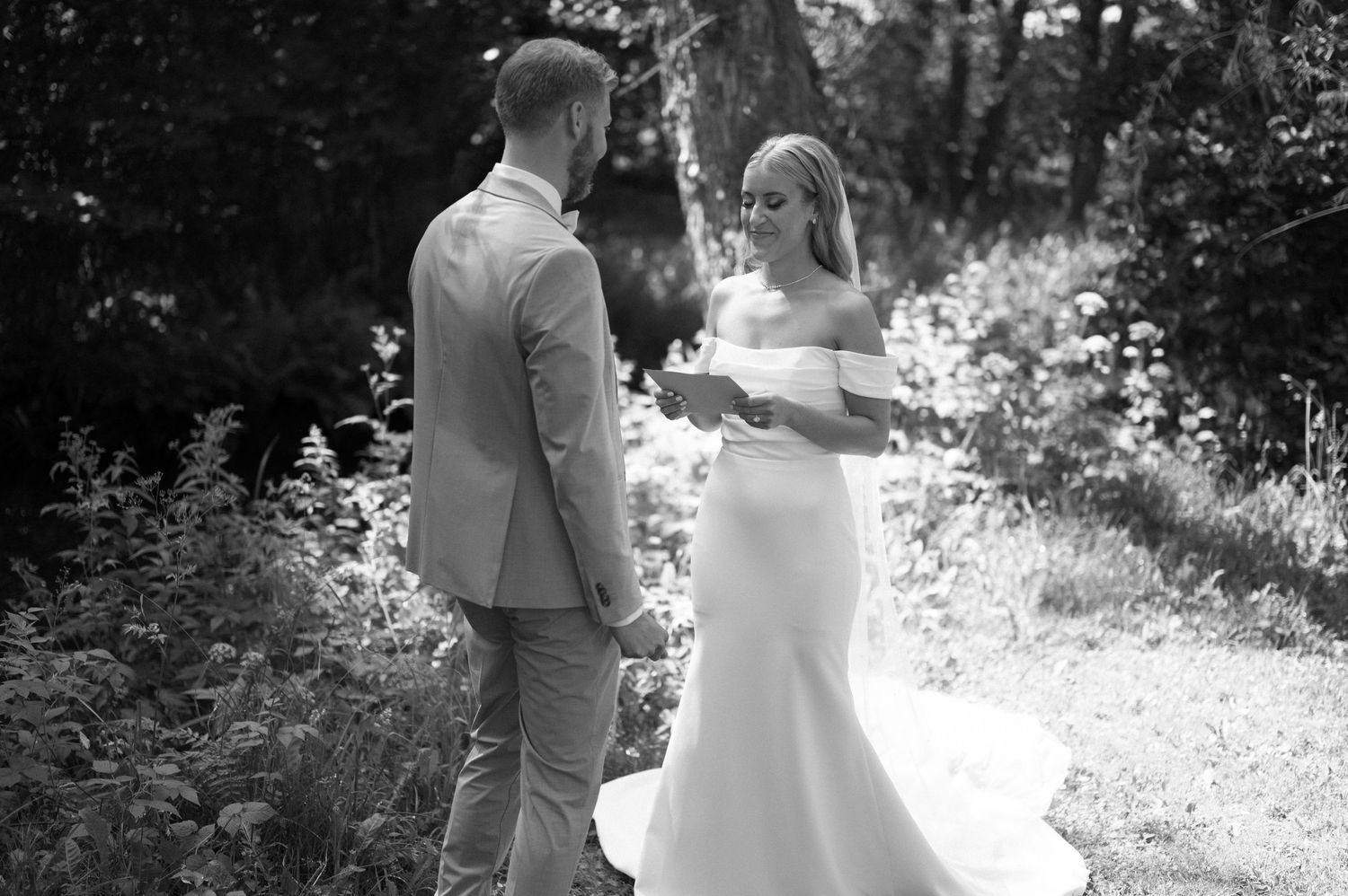 A couple exchanges handwritten letters during their first look in a wooded outdoor setting.
