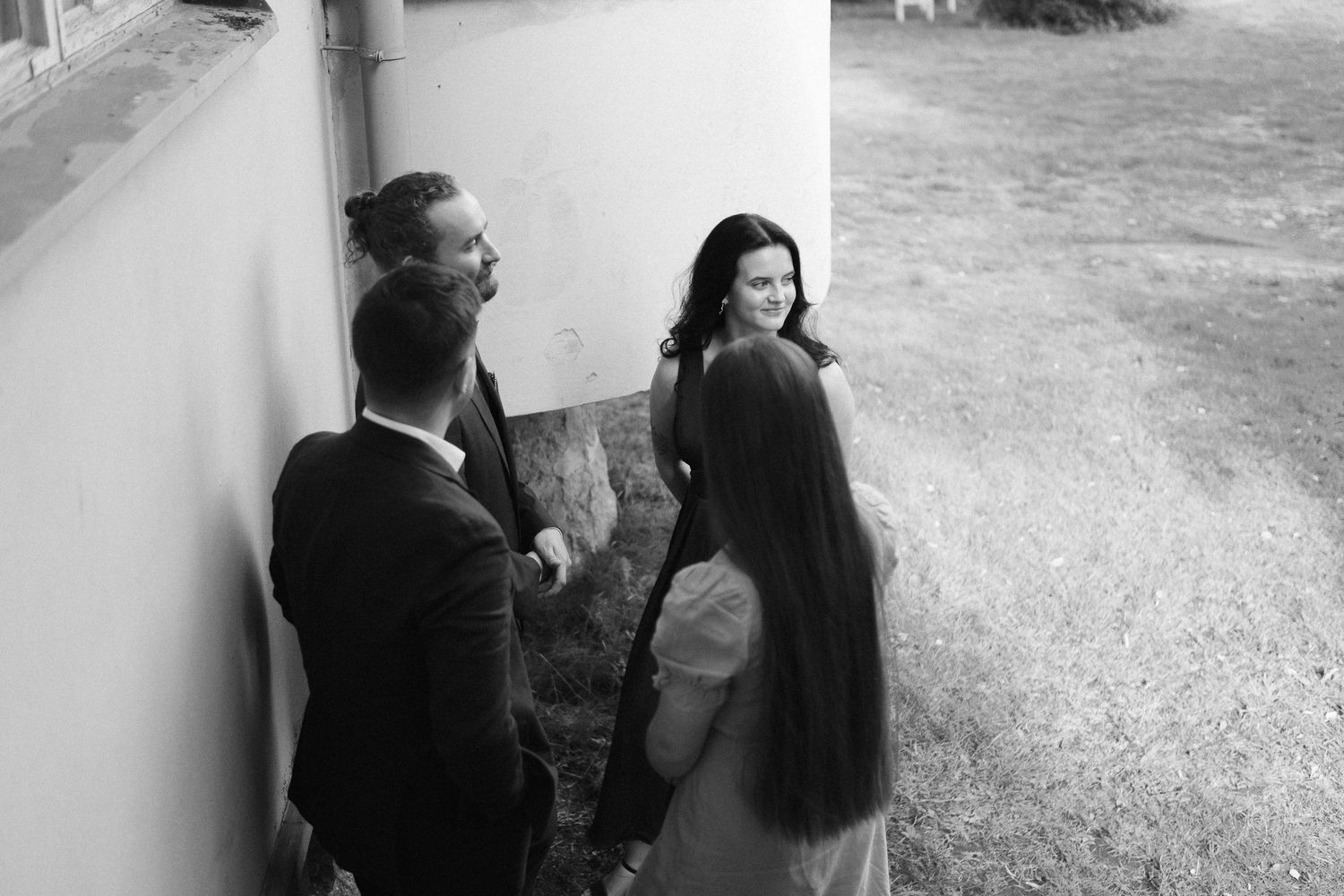 Black and white candid shot of guests conversing by a white wall outdoors.