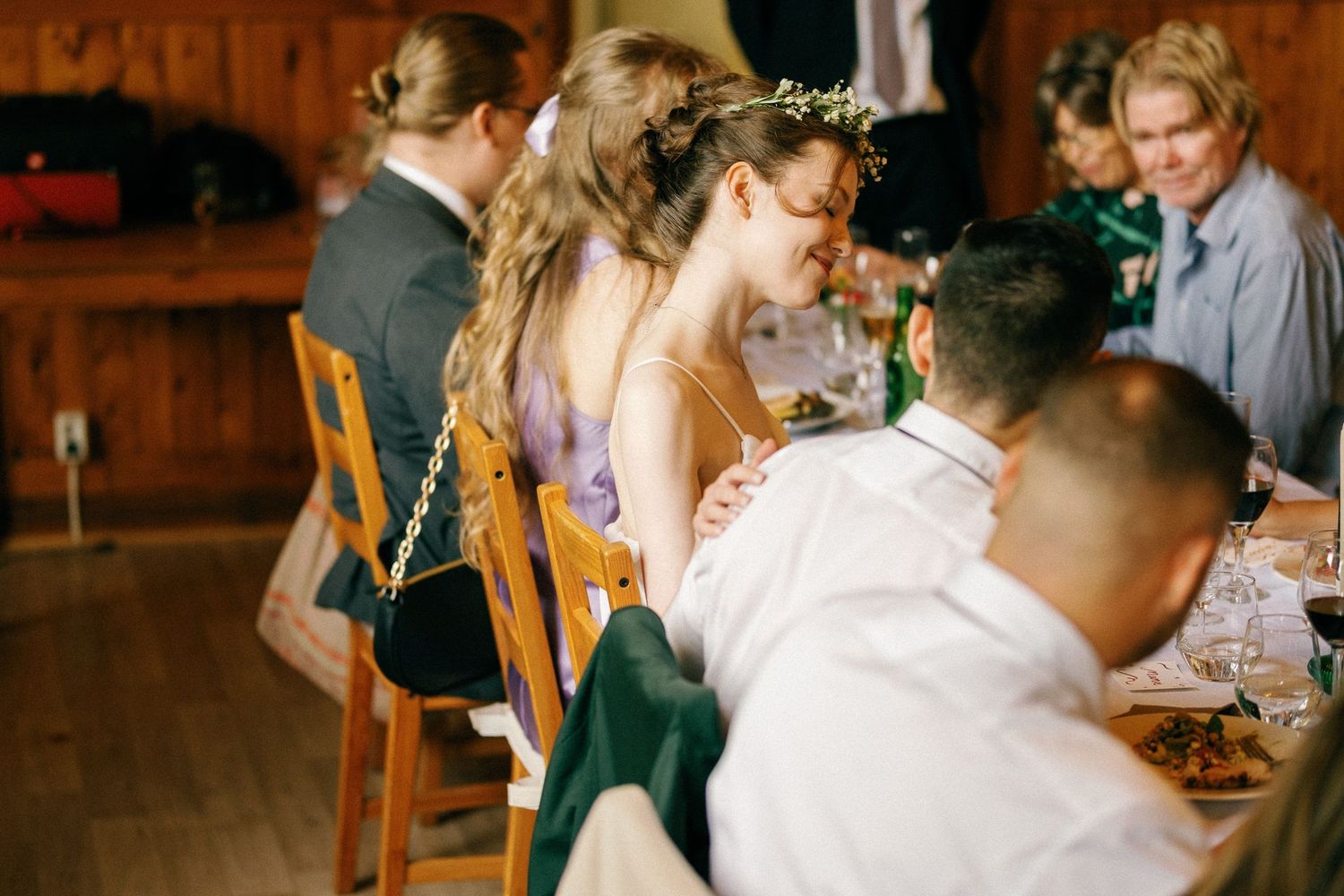 Wedding reception guests gathered around wooden tables in a warm, rustic venue setting.