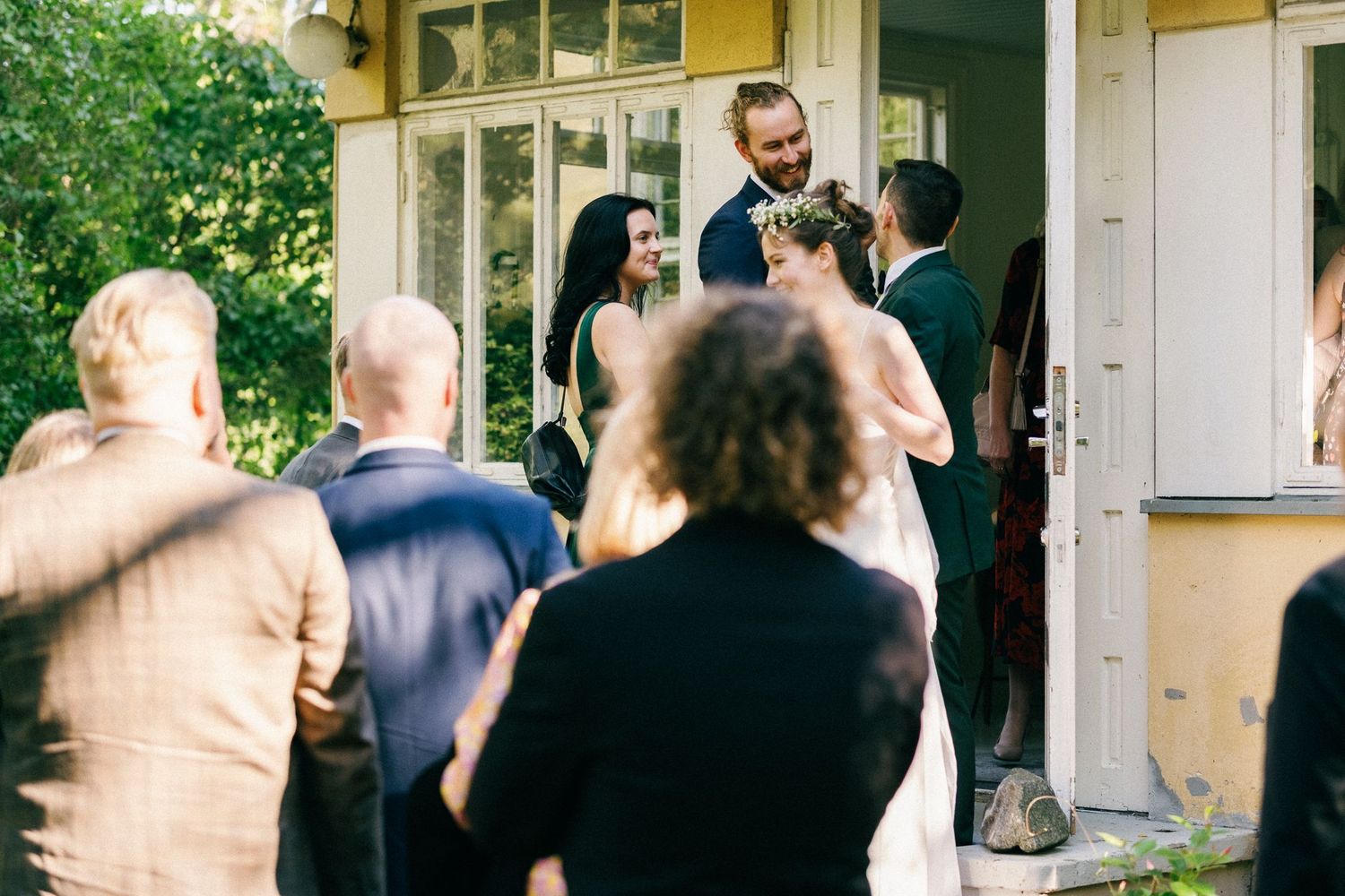 Guests socialize outside a yellow building during a wedding celebration.