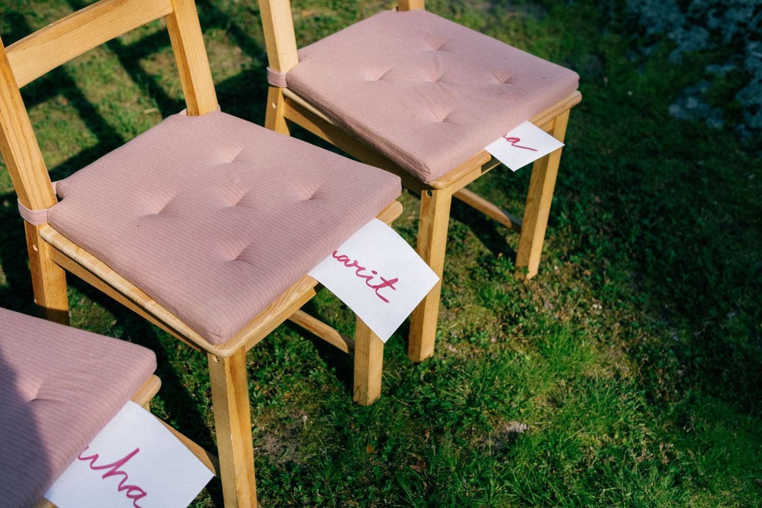 Wooden chairs with pink cushions arranged on grass with name cards.