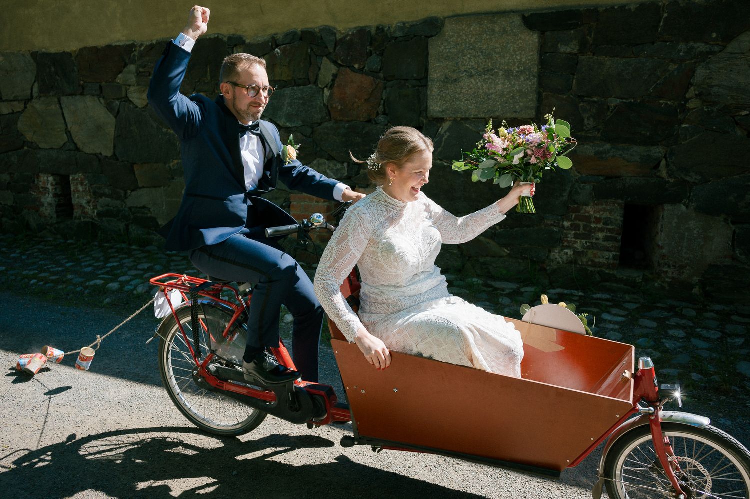 A vintage motorcycle with sidecar is used for a wedding photoshoot against a stone wall backdrop.
