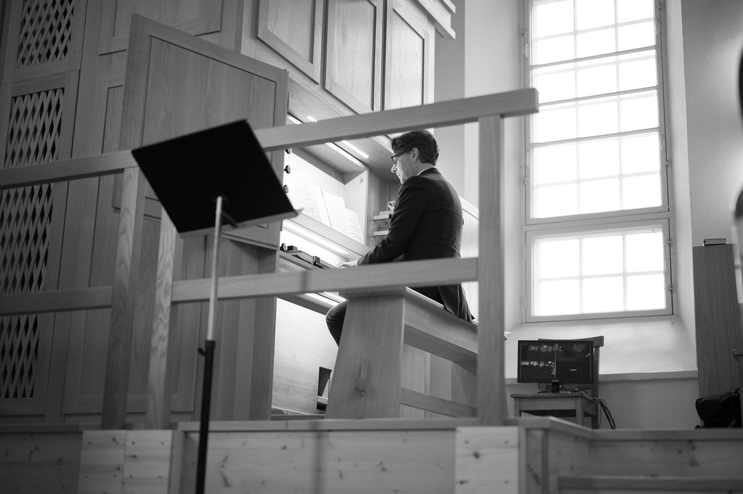 A person plays a church organ in black and white, seated at the keyboard with sheet music visible on the stand.