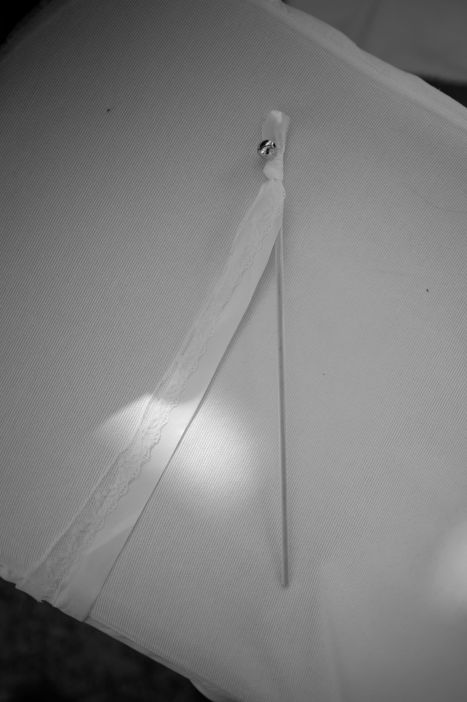 Black and white photo of a cotton swab and ribbon pinned to white fabric surface.
