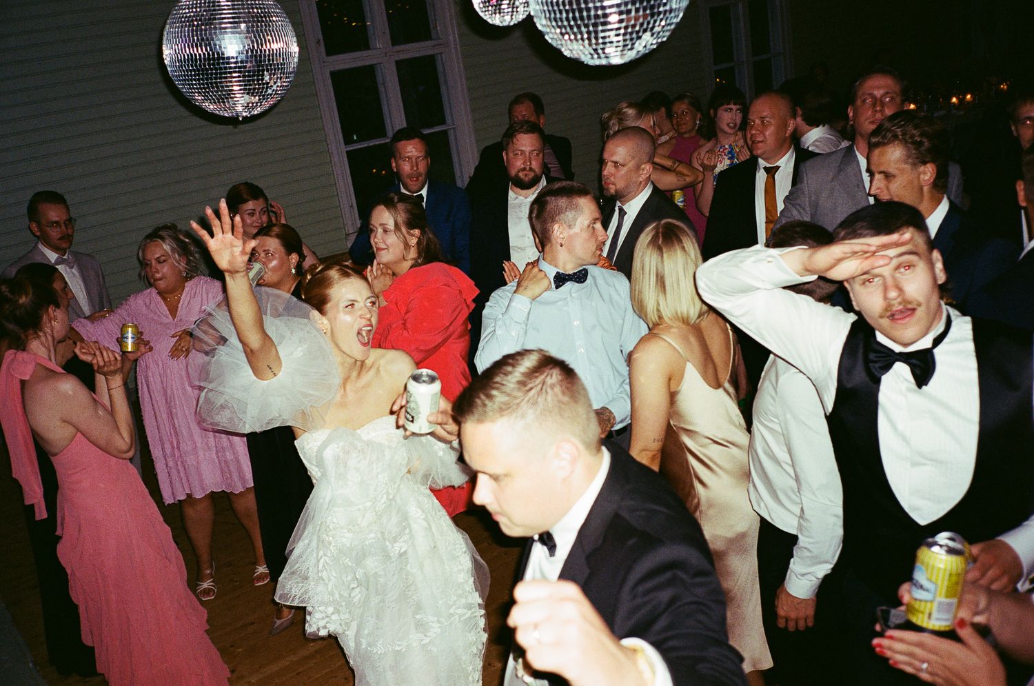 Guests dancing and celebrating at a lively wedding reception with disco balls overhead.
