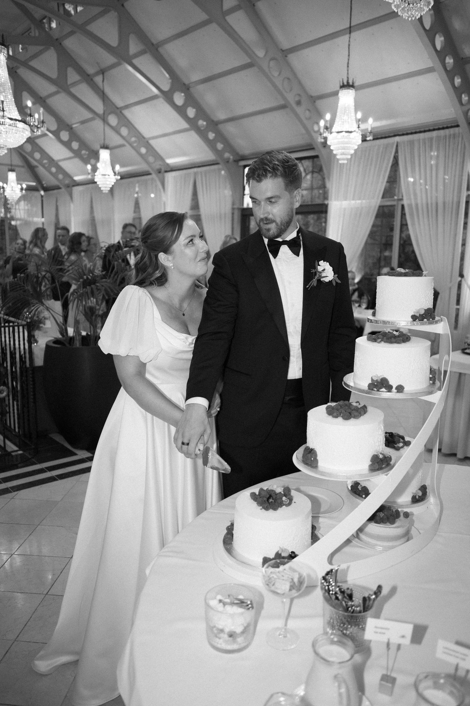Newlyweds cut their elegant white wedding cake together during reception ceremony.