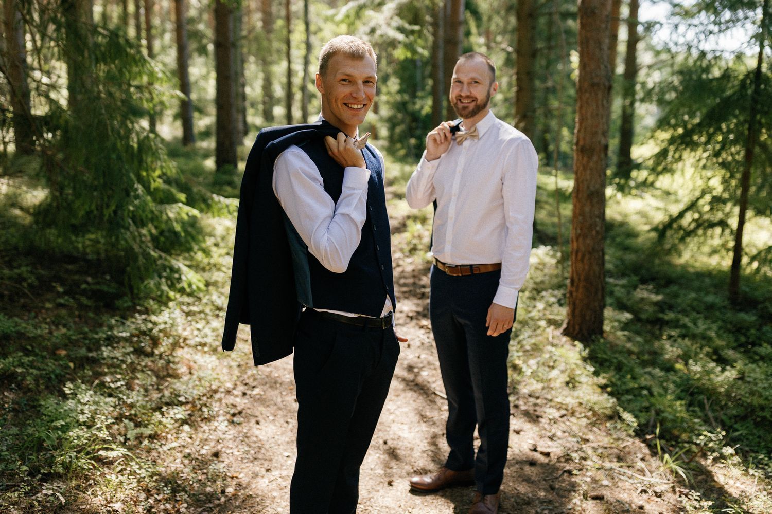 Wedding party members stand together in a beautiful wooded area.