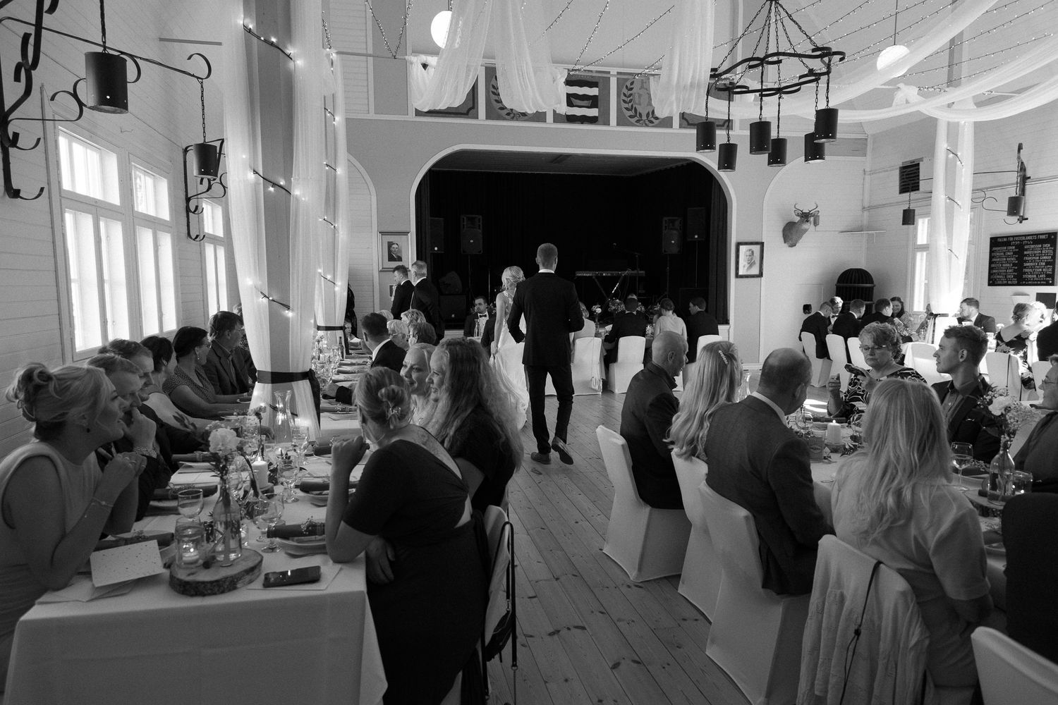 Wedding reception venue with guests seated at decorated tables in a bright hall.