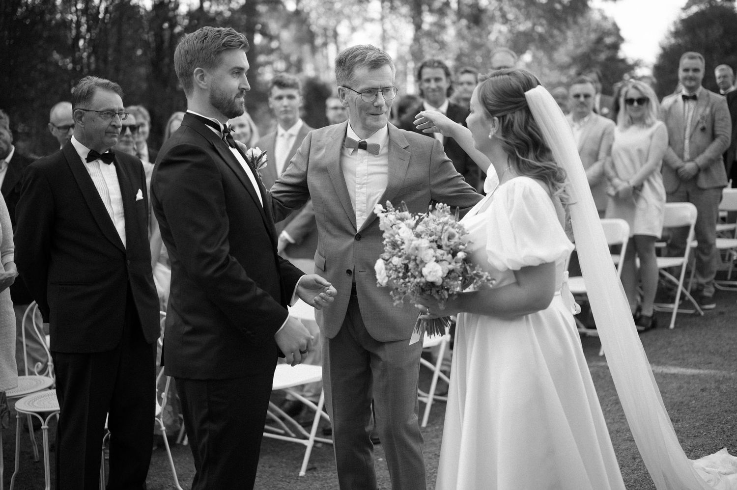 Wedding party and guests celebrate during outdoor ceremony near historic building.