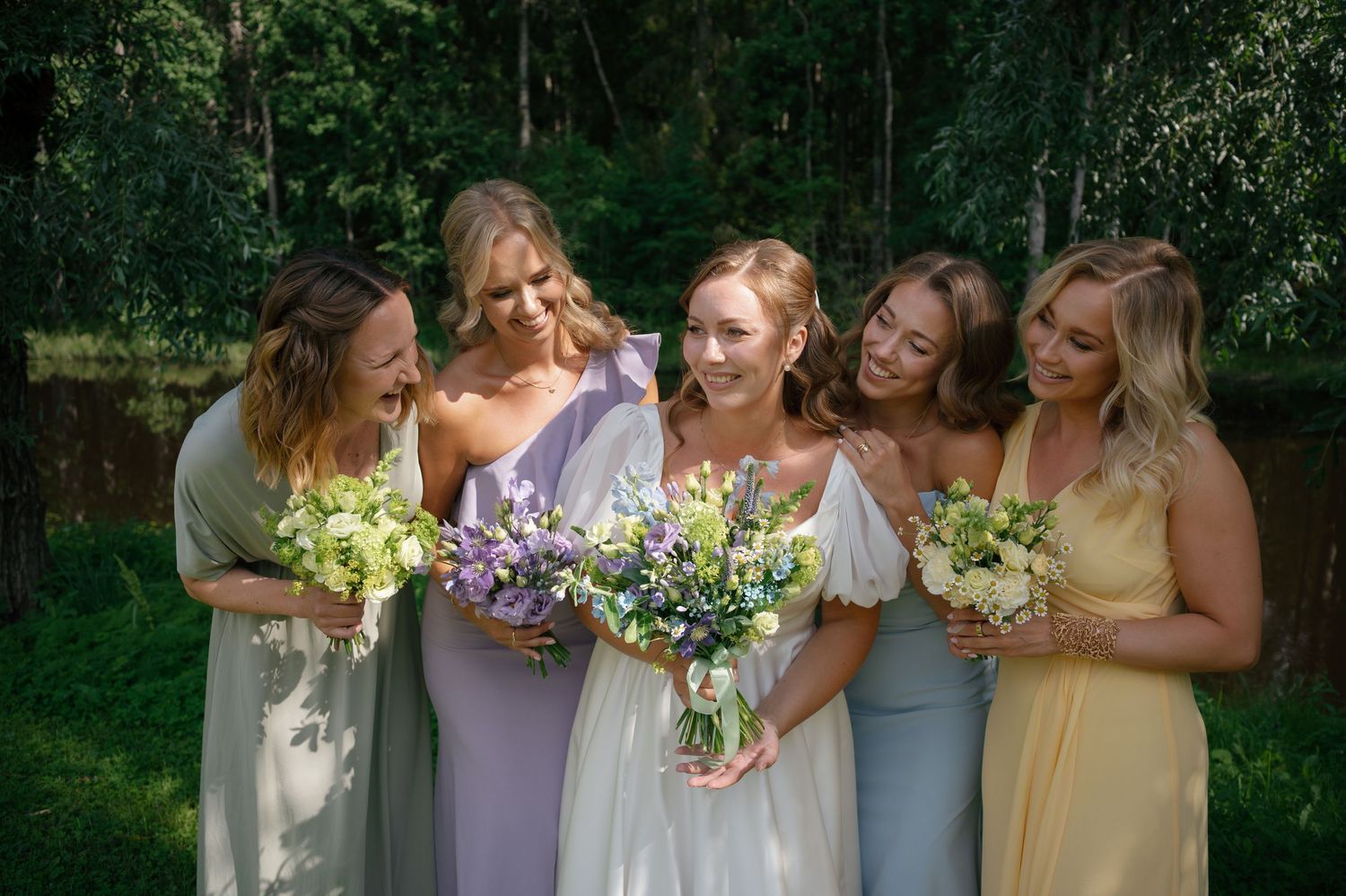 Candid moment of wedding party members laughing together while holding bouquets outdoors.
