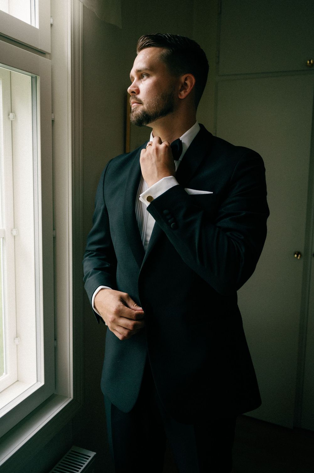 Moody portrait sequence of person in dark suit looking contemplatively out window in dramatic lighting.