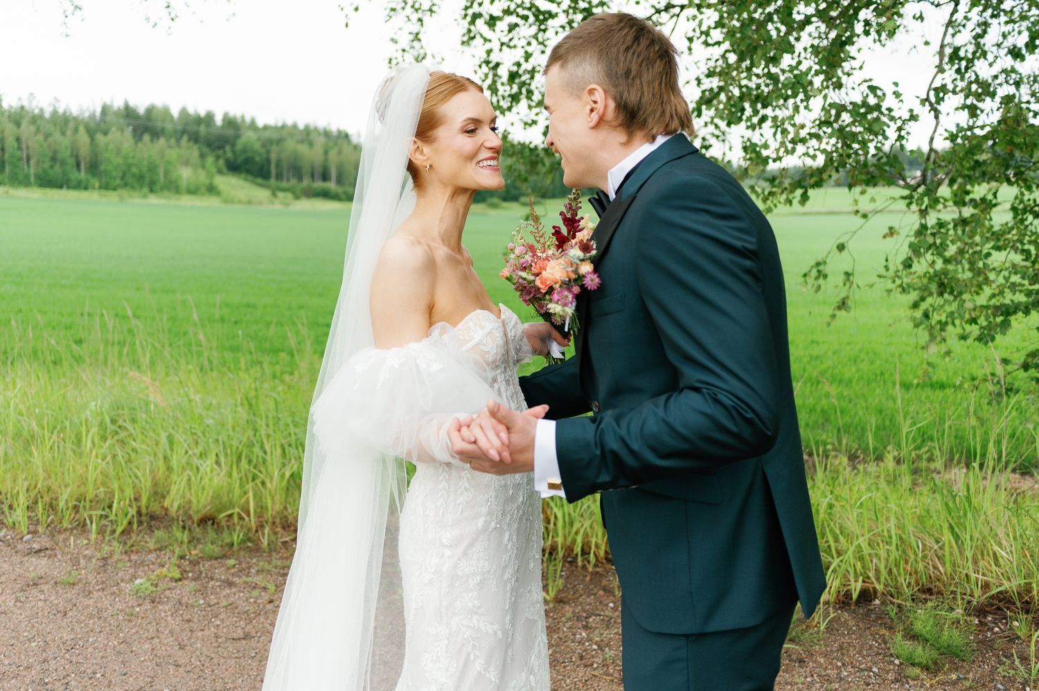 A romantic wedding moment between newlyweds on a countryside path surrounded by green fields.