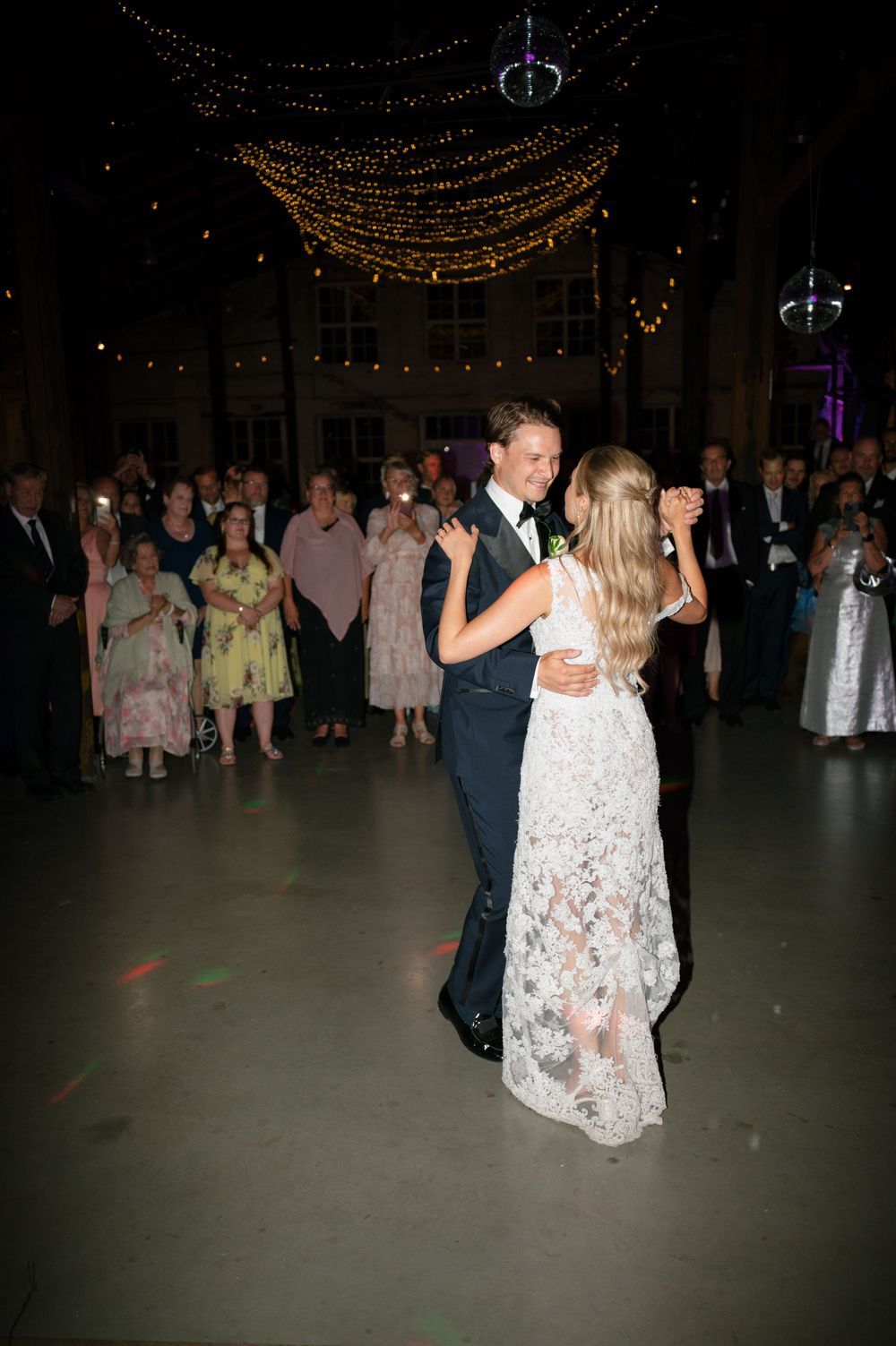 Couples dancing under string lights at an elegant wedding reception in an industrial space.